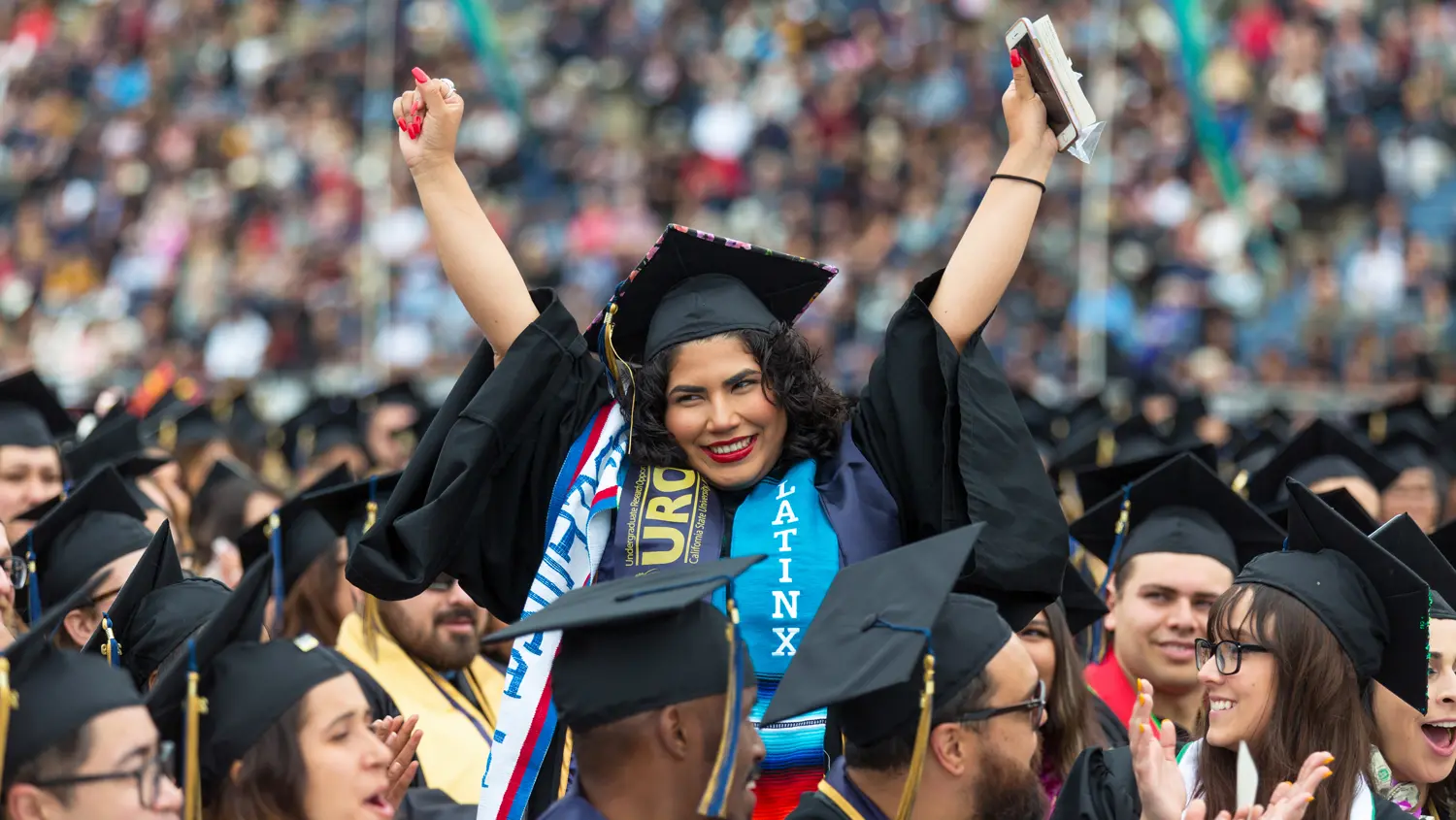 A graduate with both hands raised during commencement