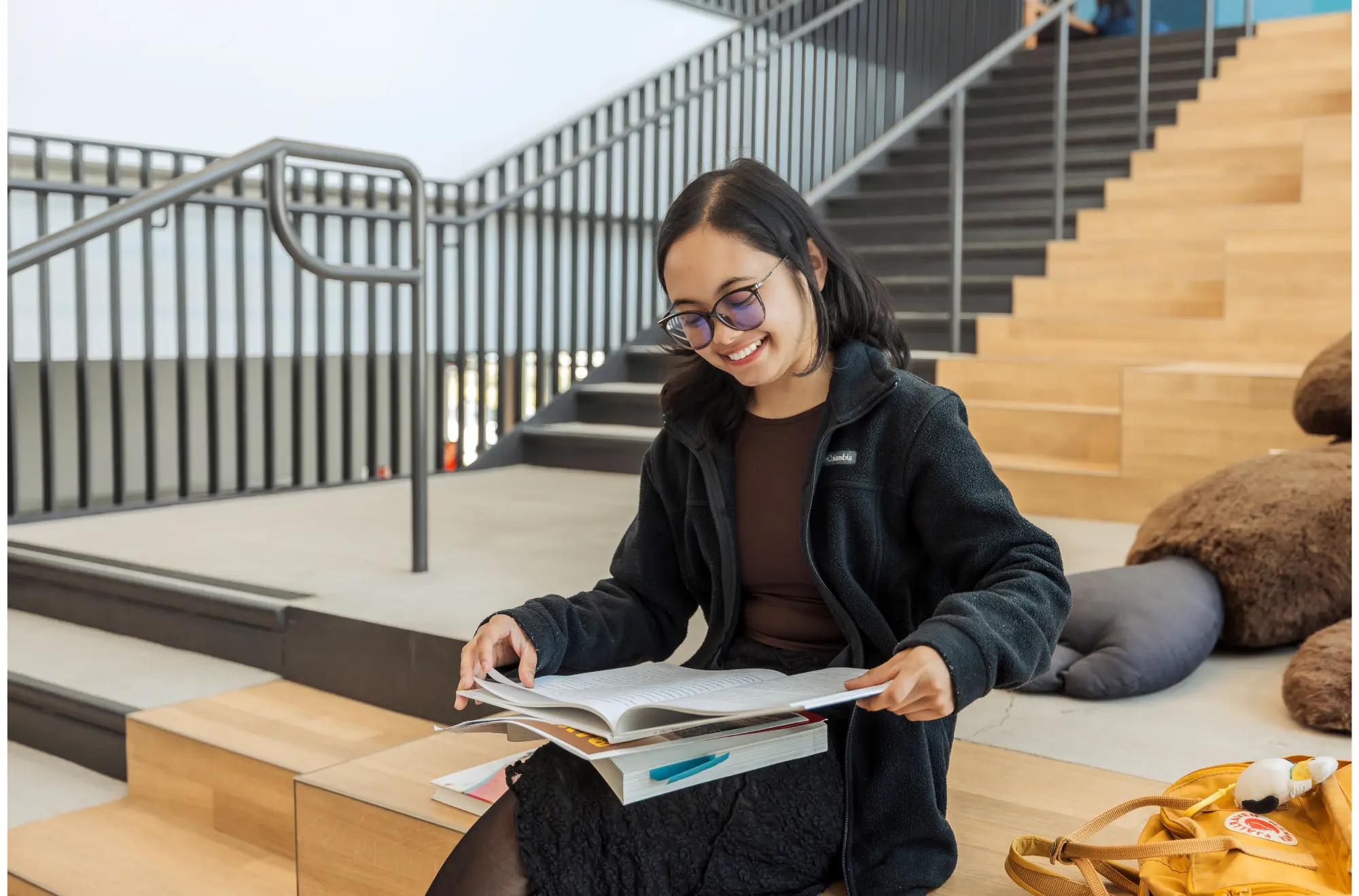 A student sitting in the OSU reading a book and smiling