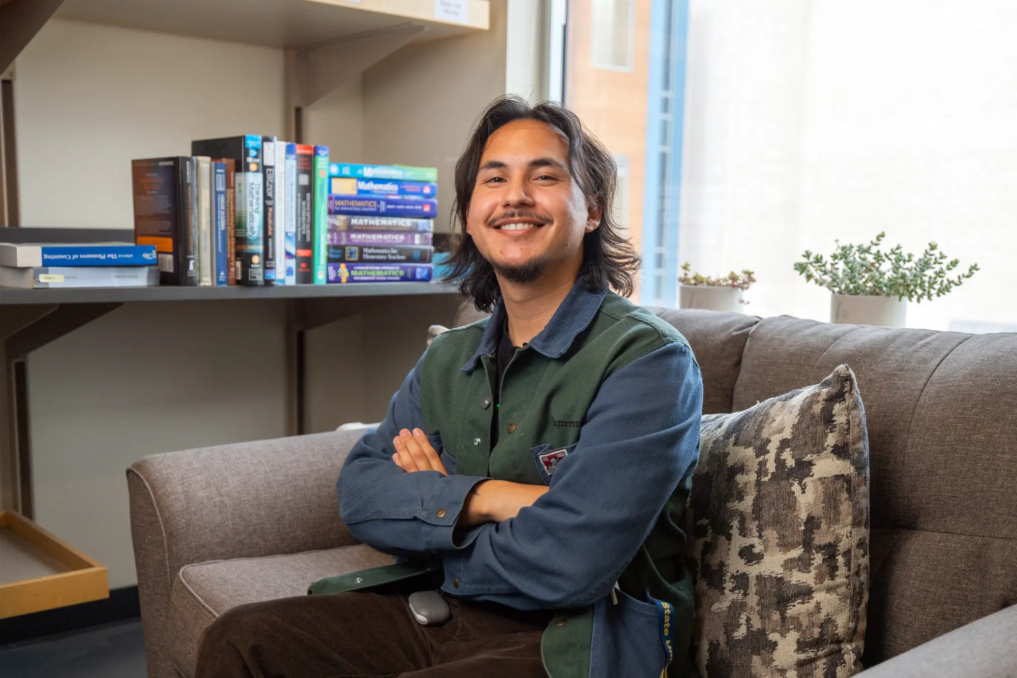 A student sitting on a couch with his arms crossed, smiling for a potrait.