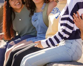 A group of students sits chatting on a bench at the beach
