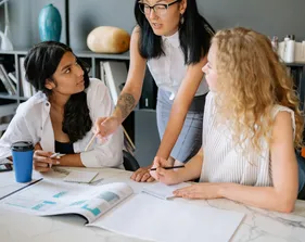 Three women at work talking at a table with documents spread out