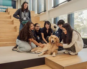 Five students sitting in front of a large monte plushe in the OSU petting Blue the therapy dog.