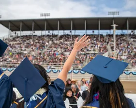 An alumni in cap and gown waves at the crowd