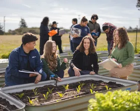 Agriculture science students and a professor engage in discussion while examining a garden bed