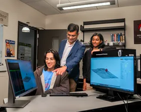 Two students and a professor looking at a computer screen and smiling at it.