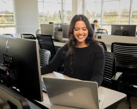 A student sitting down inside a computer lab in the business and information technology building working on their laptop