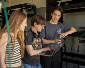 A group of students standing collaborating in the network security lab in the business and information technology building