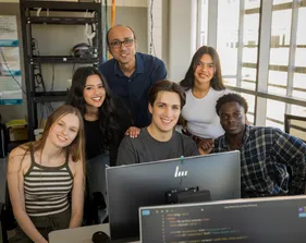 A group of students and a professor in front of a computer in the business and information technology building