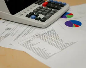 A tabletop view of printed financial documents and colorful pie charts beneath a calculator during budget review at CSUMB’s Finance Department.
