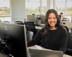 A student sitting down inside a computer lab in the business and information technology building working on their laptop