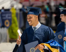 A student in cap and gown holding a diploma in his hand