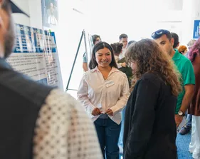 A student presenter smiles at an onlooker in the audience during her presentation