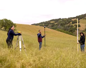 A group of three AES students setting up surveying tools in the grass