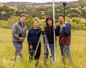 A group of four AES students holding surveying tools while smiling at the camera