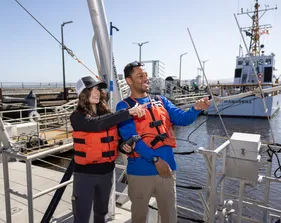 Two students on a boat with life jackets on looking out at the ocean