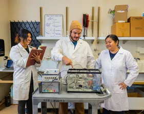 Students in lab coats observe and take notes while conducting a tank experiment in a marine science lab