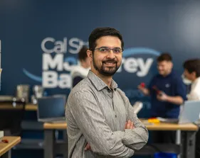A picture of a mechatronics professor smiling at the camera with students collaborating in the background
