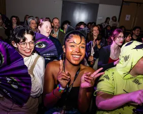 Students cheer and wave purple fans in a packed room during CSUMB’s Werk Witch event.