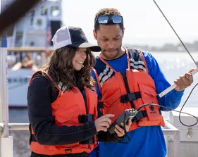Two students on a boat with a life jacket collaborating together