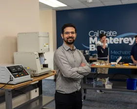 A picture of a mechatronics professor smiling at the camera with students collaborating in the background