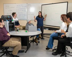 A professor giving a presentation to students sitting by a 3d printer
