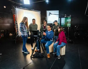 Group of students smiling while standing around the camera and watching it