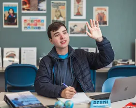 A student raising his hand while having a computer open