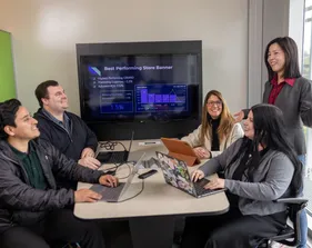 A business administration professor giving a presentation to a group of four students