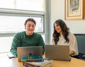 A masters of business administration student and professor sitting down together at a table collaborating