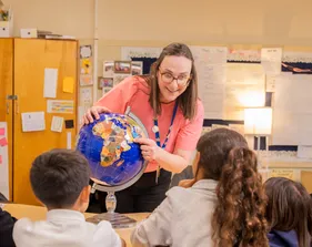 Teacher showing a globe to students sitting around a table in a classroom