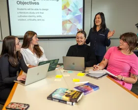Four students sitting at a table listening to their professor teach them.