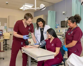 A group of three nursing students in scrubs and a professor collaborating to practice testing blood pressure