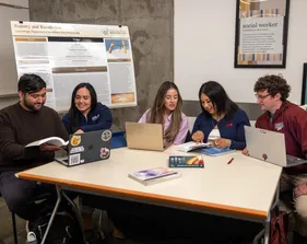 A group of five social work credential students sitting down at a table and collaborating together
