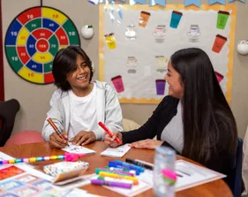 A social work credential student sitting in a classroom with a kid collaborating with them