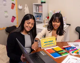 A social work credential student sitting in a classroom teaching a kid while the kid points at the laptop