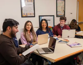 A group of five social work credential students sitting down at a table listening to one talk