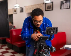 Film crew member bent down looking at the camera being used for filming