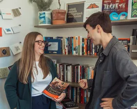 Professor holding a book while smiling at a student and the student is smiling at the book.