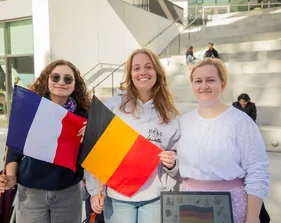 Three students standing together two holding flags