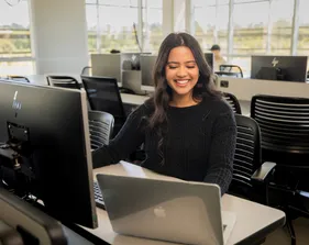 A student sitting down inside a computer lab in the business and information technology building working on their laptop