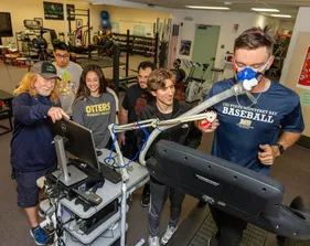 Student on treadmill with oxygen mask on with plenty of students watching him
