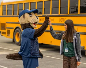 Mascot high fiving a student in front of a bus