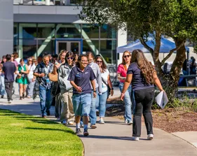 A group of people walk together outdoors on a sunny day, smiling and chatting as they take part in a campus or community event.