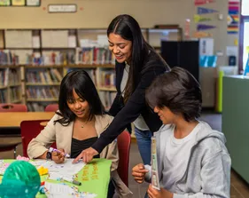 Social work student helping two children in a classroom.
