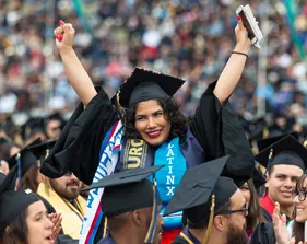 A graduate with both hands raised during commencement