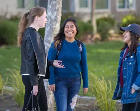 Three students talking and smiling outside.