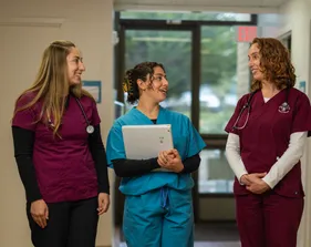 A group of three nursing students in scrubs standing together in a walkway talking together