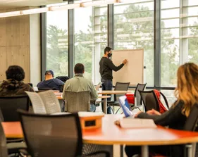 Instructor writing on a whiteboard while students listen in a classroom.