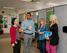 Four members of the human resources department stand in an office chatting and smiling.