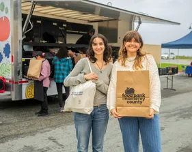 Two students smile and hold up food they received from the food bank